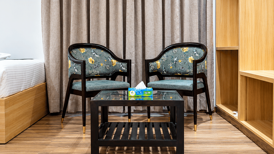 Seating corner in a room at Daksh The Royal Braj, Vrindavan, with two patterned armchairs, a glass-top coffee table, and curtains.