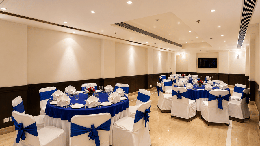 Banquet hall set up with round tables dressed in white and blue linen, patterned chair covers and warm ambient ceiling lighting throughout.