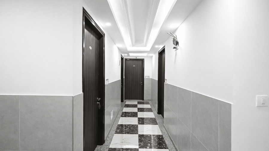 A corridor at Hotel Apple Park Delhi featuring chequered floor tiles, and recessed ceiling lighting.