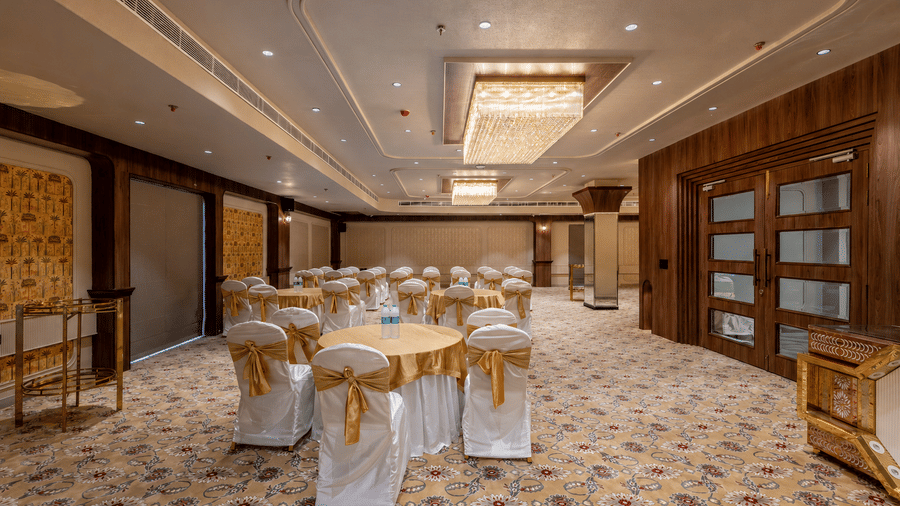 Banquet hall arranged with round tables, covered chairs, and decorative lighting.