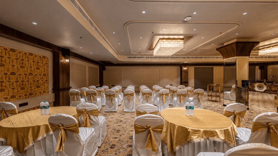 Banquet hall with round tables, covered chairs, floral decorations, and patterned carpet.