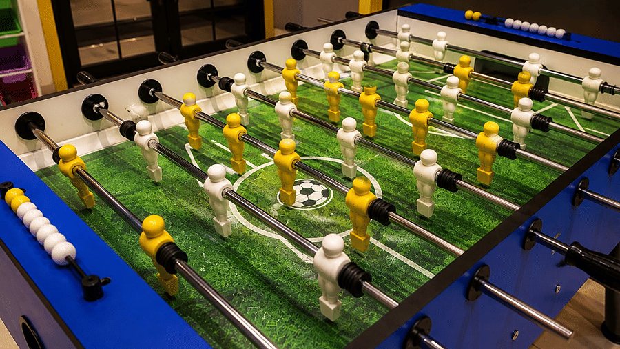 A close up view of a foosball table at Hotel Sonar Bangla, Mayapur, featuring miniature player figurines, control rods, and a pitch pattern.