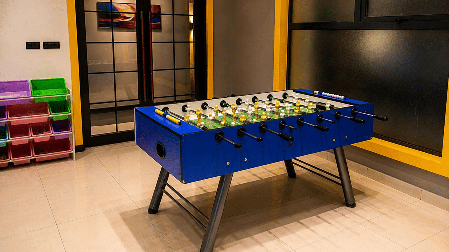An indoor play area at Hotel Sonar Bangla, Mayapur, featuring a foosball table, a tiled floor, and glass panel windows.
