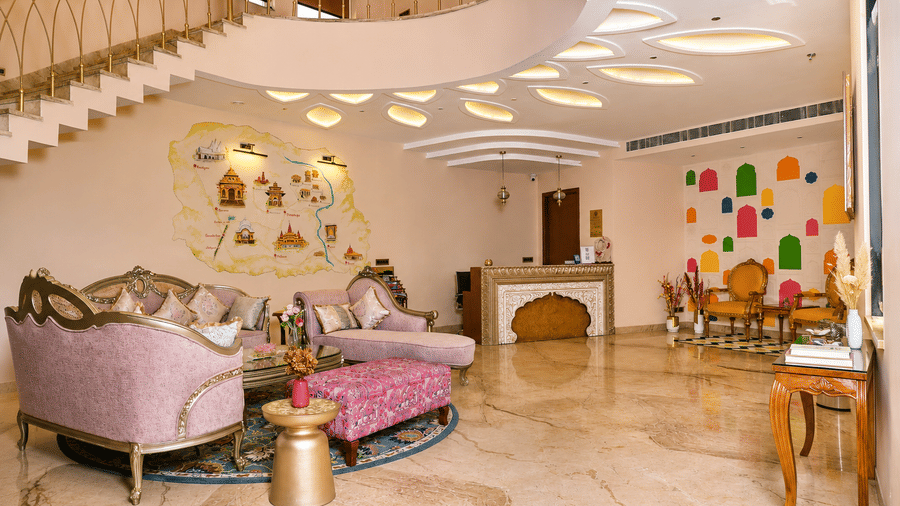 Guest lounge with pink sofas, a curved staircase, and decorative ceiling lighting at Kadamb Kuteer, Vrindavan.