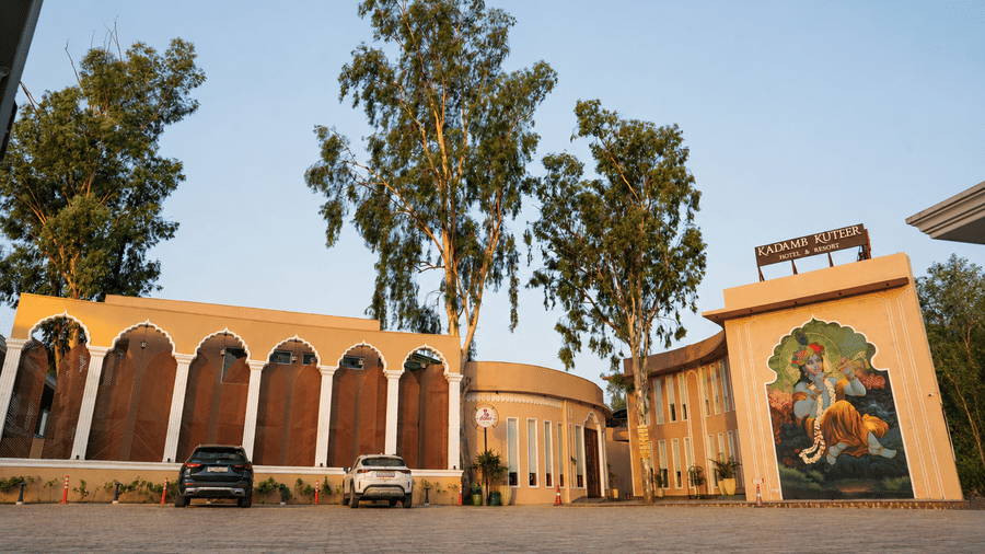 Daytime exterior view of the property with arched architecture, murals, and mature trees at Kadamb Kuteer, Vrindavan.