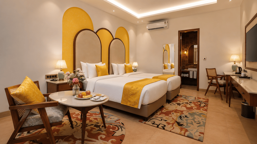 Spacious guest room with an arched headboard, yellow accents, floral carpet, and a seating area at Kadamb Kuteer, Vrindavan.