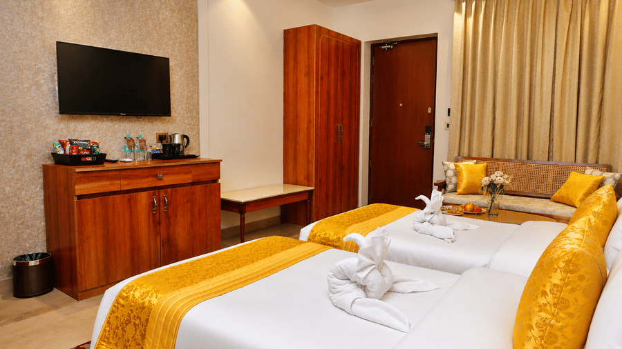 Guest room with a wall-mounted TV, wooden wardrobe, and a white bed with a yellow runner at Kadamb Kuteer, Vrindavan.