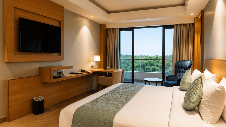 Bedroom featuring wall-mounted TV, desk, and balcony view in the Grand Suite at Kiranshree Grand Hotel.