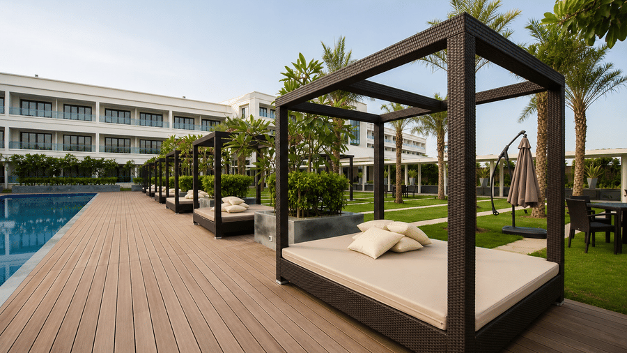 Wooden poolside cabanas with plush cushions on the outdoor deck at Kiranshree Grand Hotel.
