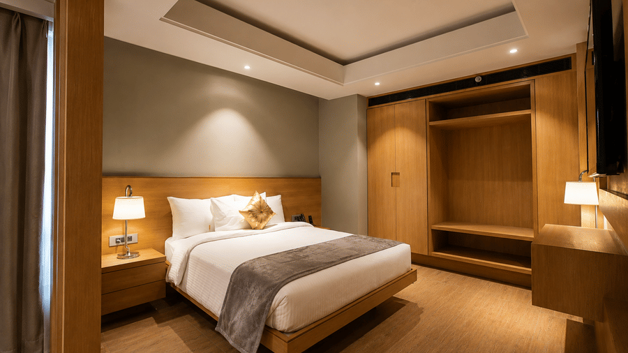 Spacious bedroom with a double bed and wooden wardrobe in the Presidential Suite at Kiranshree Grand Hotel.