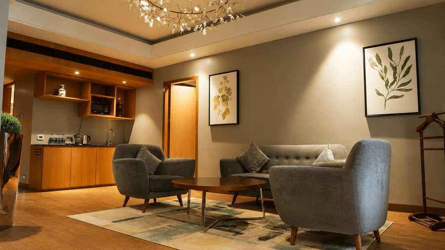 Elegant living room featuring plush armchairs, sofa, and kitchenette in the Presidential Suite at Kiranshree Grand Hotel.