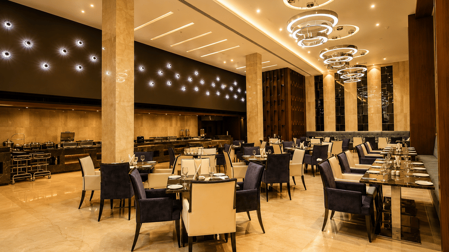 Elegant dining room featuring set tables and modern ring chandeliers at Kiranshree Grand Hotel.