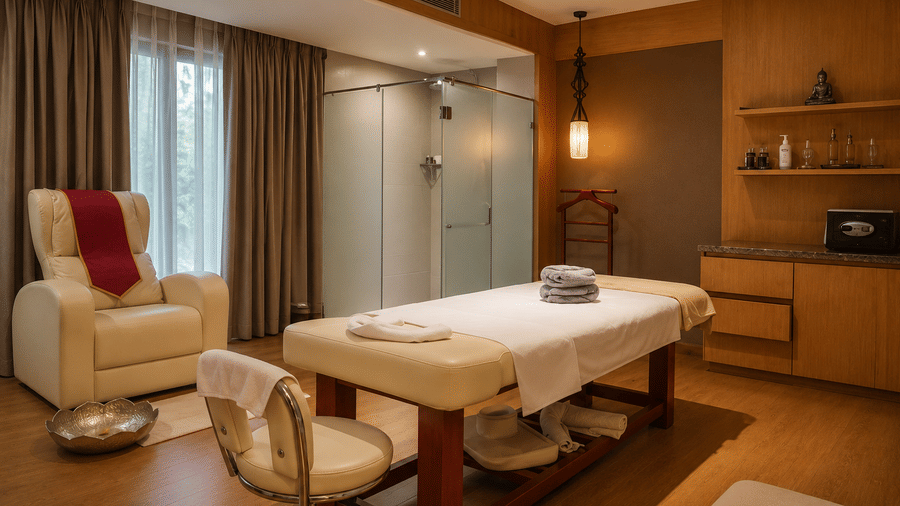 Spa treatment room with a massage bed, recliner chair, and shower at Kiranshree Grand Hotel.