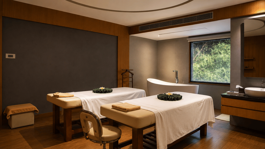 Couples spa treatment room with two massage tables and bathtub at Kiranshree Grand Hotel.