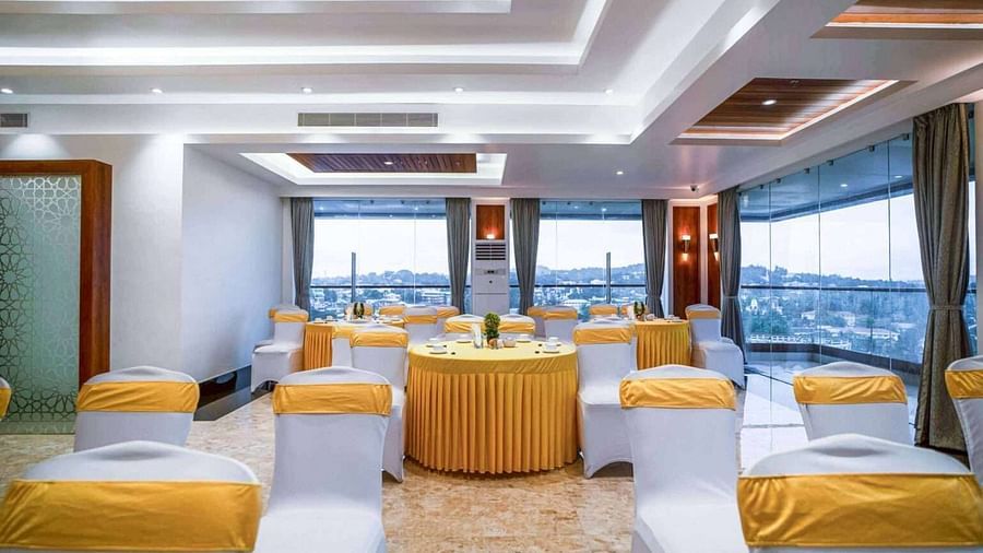 A brightly lit event space at Mansha Palace is set up with round tables and draped chairs, offering a city view.