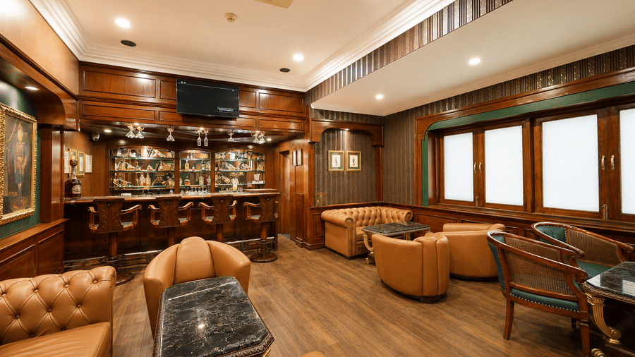 Cavalry Bar with backlit bottle shelves, carved wooden stools, tan leather seating, marble-topped tables and wood panelling at MAYFAIR Garden, Rourkela.