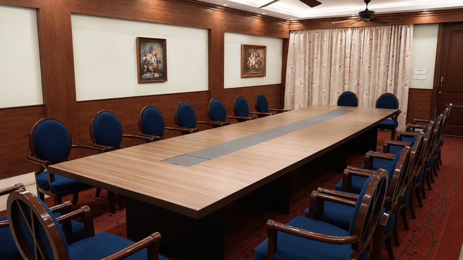 Camellia board room with a long wooden conference table, blue high-back chairs, panelled walls and floral paintings at MAYFAIR Himalayan Spa Resort, Kalimpong.