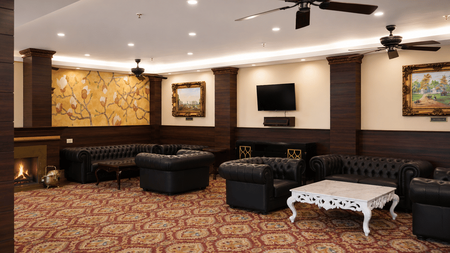 Drawing Room lounge with black leather Chesterfield sofas, a lit fireplace, a floral wall mural and a carved coffee table at MAYFAIR Himalayan Spa Resort, Kalimpong.