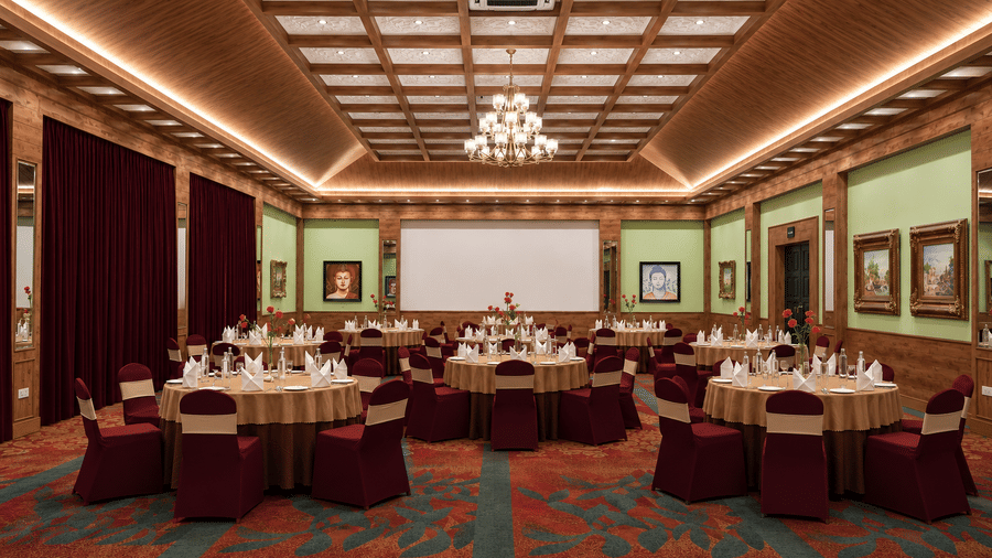 Everest Hall set for a banquet with round tables, maroon chair covers, a projector screen and a chandelier at MAYFAIR Himalayan Spa Resort, Kalimpong.