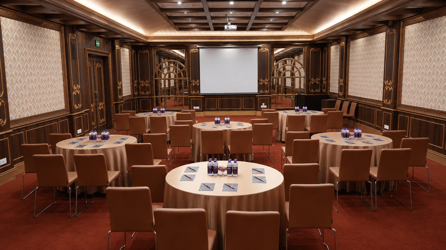 Kanchenjunga Hall arranged with round tables and chairs facing a projector screen, with damask wall panels at MAYFAIR Himalayan Spa Resort, Kalimpong.