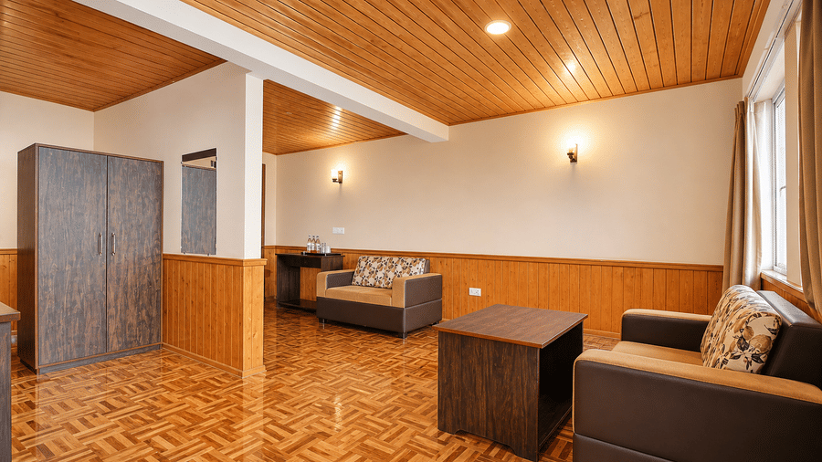 The lounge area of the Junior Suite at Orsino Khangri Karpo Retreat & Spa, Lachung contains sofas and a table. A wardrobe stands against the wall. Lights are fixed to the ceiling.