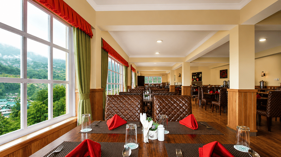 Orion restaurant featuring a view from a table showing place settings in the foreground. A row of windows runs along the wall next to tables and chairs. 