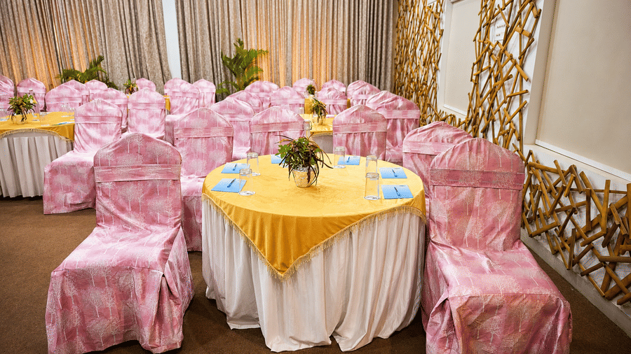 Banquet hall with round tables dressed in yellow and white linen, pink patterned chair covers and decorative bamboo lattice wall panels nearby.