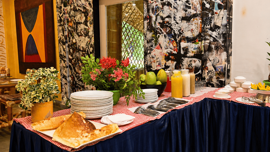 Restaurant buffet spread laid out on a dark blue tablecloth with fresh flowers, fruit juices, bread rolls and plates arranged neatly on top.