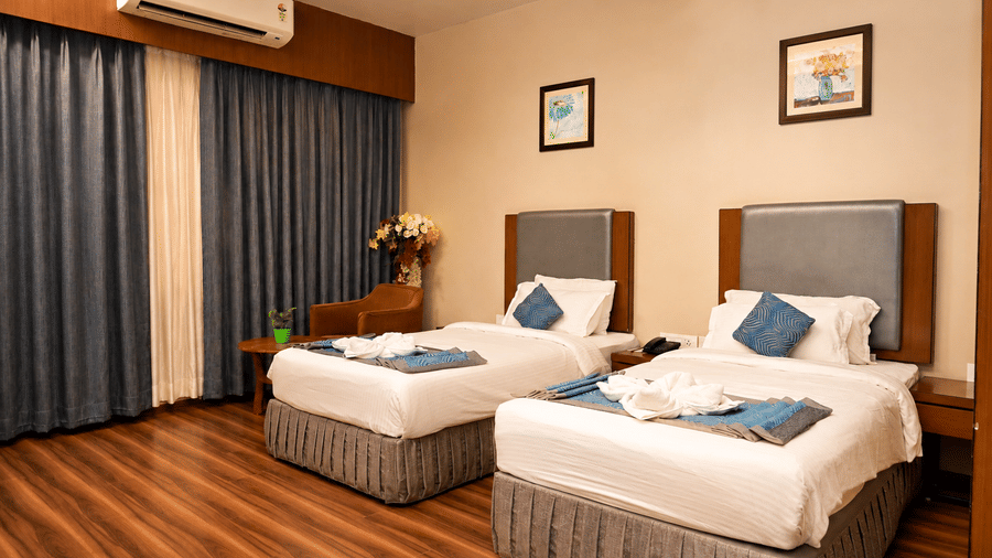 Club Superior Room with twin beds, striped curtains, and warm wooden flooring at Pipul Padmaja Premium Hotel, offering comfort.