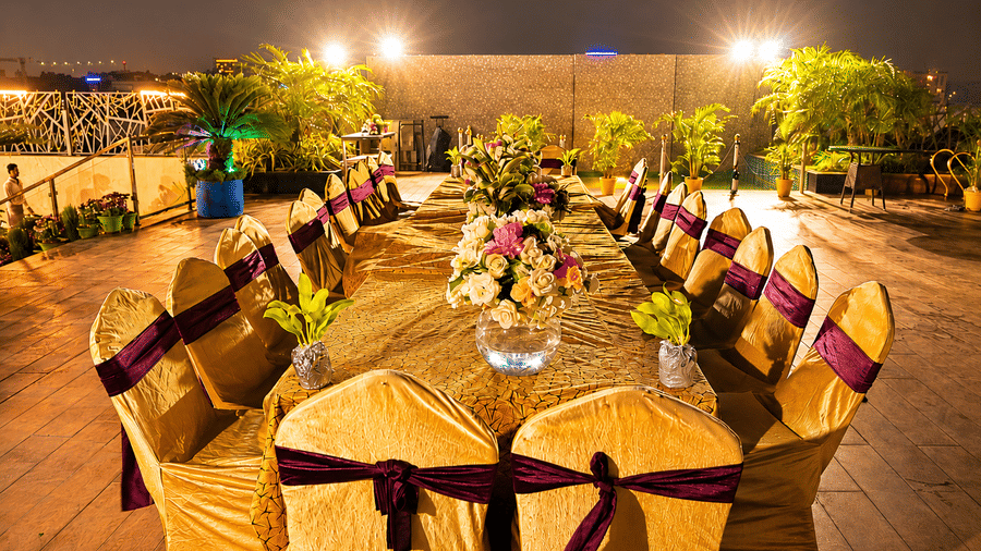Outdoor poolside deck set up at night with a long banquet table, gold chair covers with purple sashes and floral centrepieces along the table.