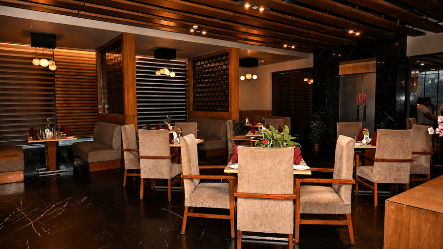Restaurant dining area with wooden tables and upholstered chairs, an exposed wooden beam ceiling, warm lighting and dark polished flooring.