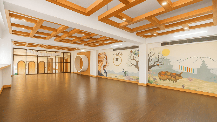 An indoor view of a spacious, empty room or conference hall with decorative wooden ceiling beams, hardwood floors, and a scenic wall mural in a hotel in Sikkim.