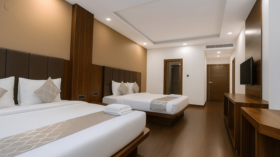 A clean, modern hotel room viewed from the foot of the bed, showing a wall-mounted TV and a hallway entrance.