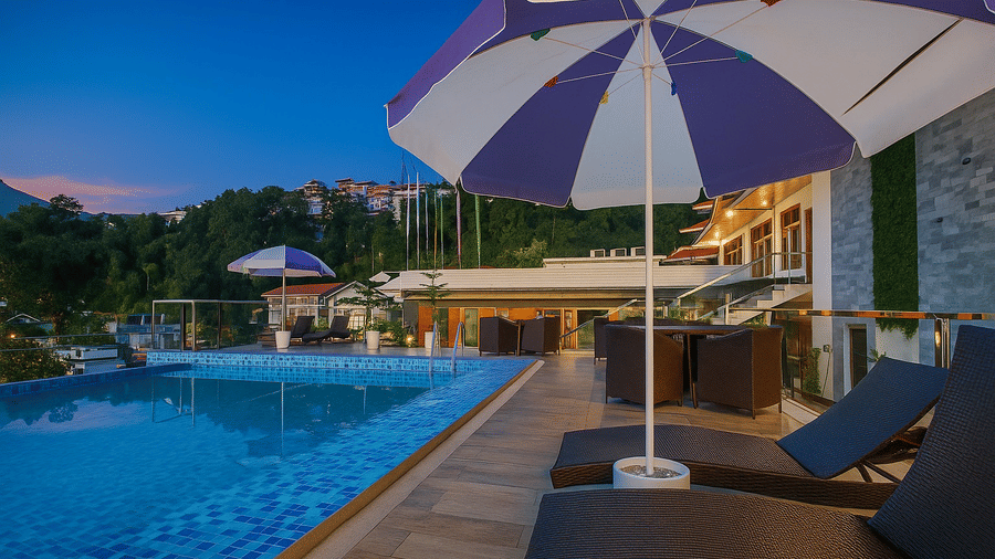 The Royal potala by orsino pool deck featuring lounge chairs under umbrellas, overlooking a swimming pool and mountains during the twilight hours.