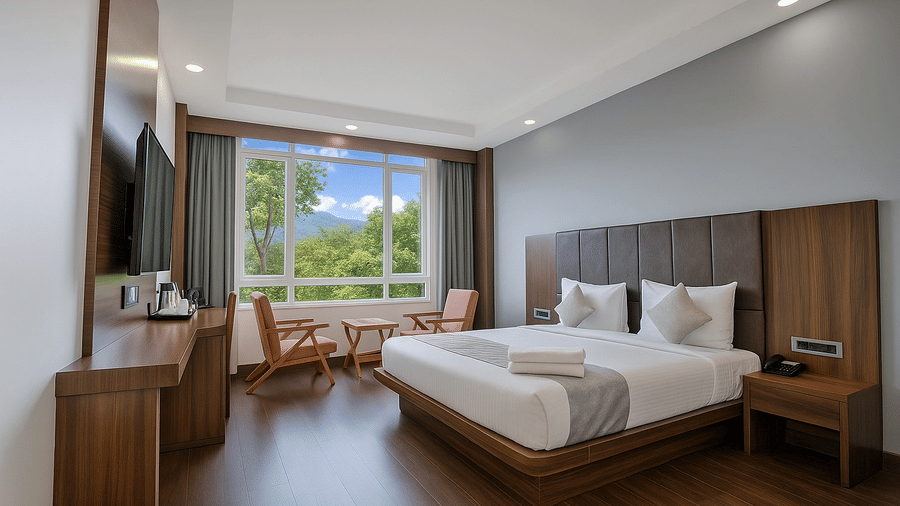 A bright hotel room showing a bed, a desk area, and a large window with a view of the mountains.