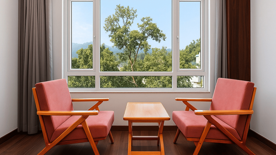 Two coral-colored armchairs and a small wooden coffee table positioned in front of a large window overlooking green trees.