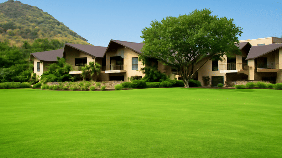 A well-manicured lawn stretches in front of a building complex, set against a backdrop of hills | Wedding Garden | The Qualia Resort Club & Brewery, Udaipur