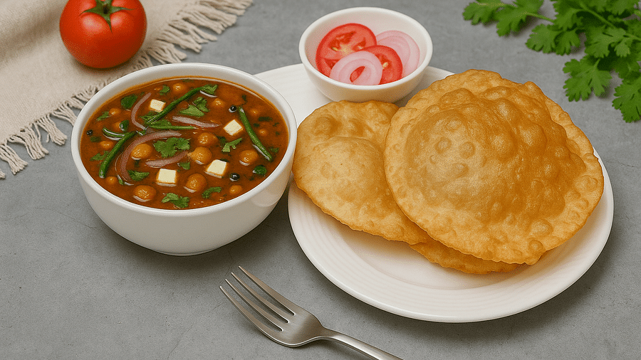 Bowl of chole with two bhature, salad, and a tomato placed beside the plate at Tisya Farms, Gurgaon.