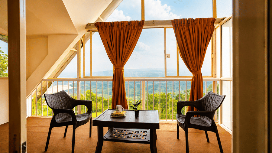Sunlit balcony alcove at Wind Chalet with two black armchairs, small coffee table, orange drapes, and a scenic view.
