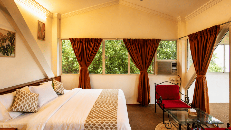 Spacious Wind Chalet bedroom featuring a double bed, bedside table, red armchairs, ceiling fan, and large windows.