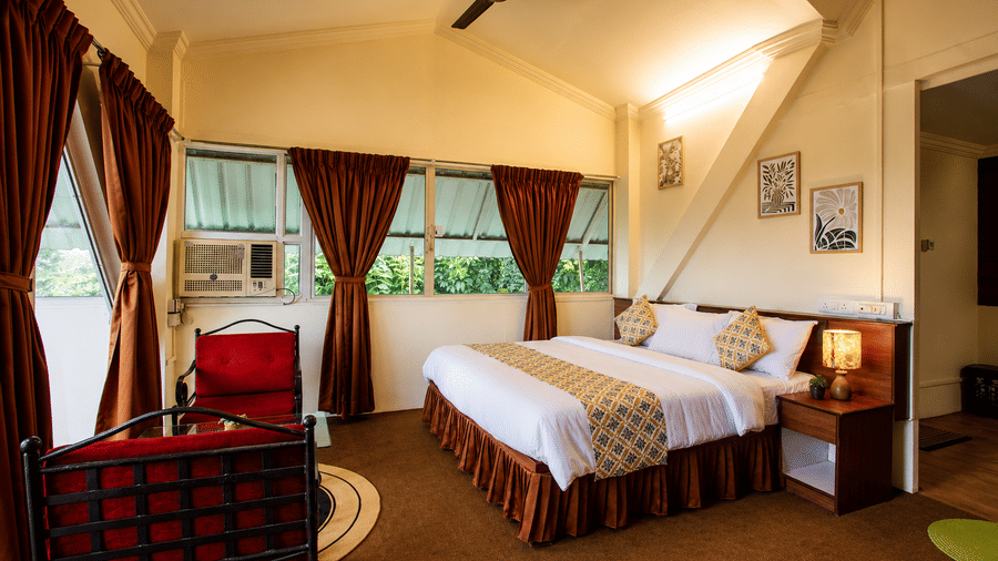 High-angle view of a Wind Chalet bedroom showing a double bed, ceiling fan, red armchairs, and long brown drapes.
