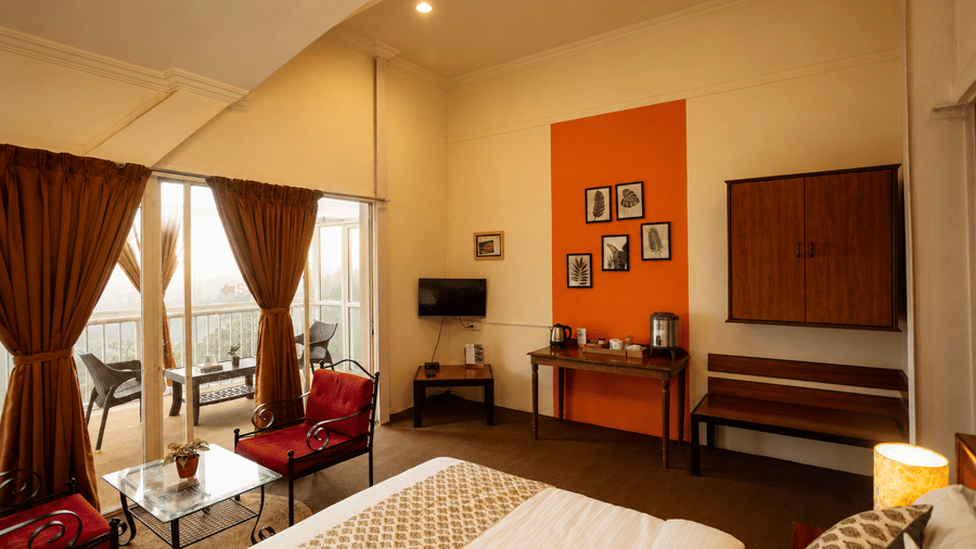 Wide room perspective at Wind Chalet showing a made double bed, red armchair, orange feature wall, and balcony access.