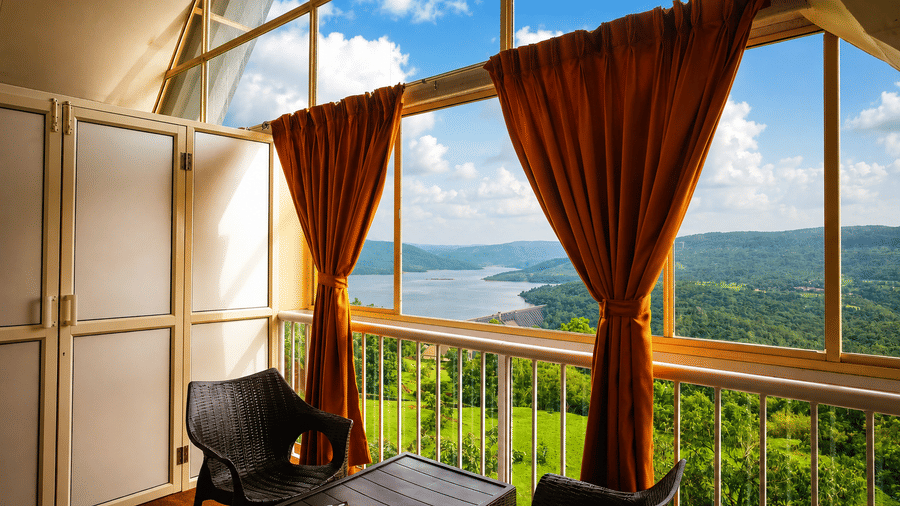 Covered terrace at Wind Chalet with seating overlooking lush green hills and a blue lake under a clear sky.