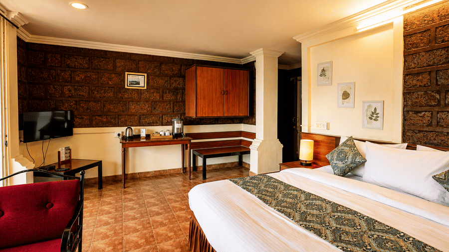 Spacious guest suite at Wind Chalet featuring tiled floor, double bed, wooden cabinet, desk, and red armchair.