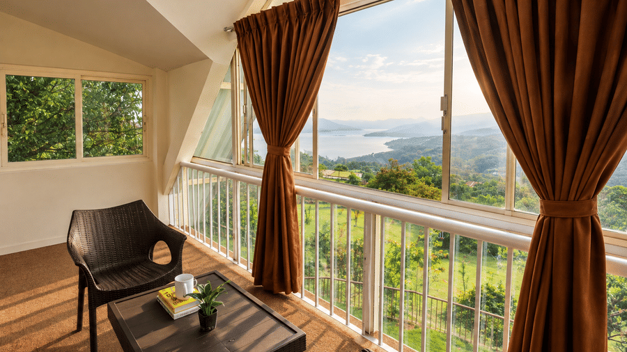 Enclosed balcony at Wind Chalet with table, armchair, brown drapes, and large windows with panoramic valley views.