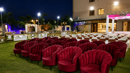 Rows of velvet red armchairs are neatly arranged on an outdoor lawn for an event - Lords Inn Sangam, Bhopal