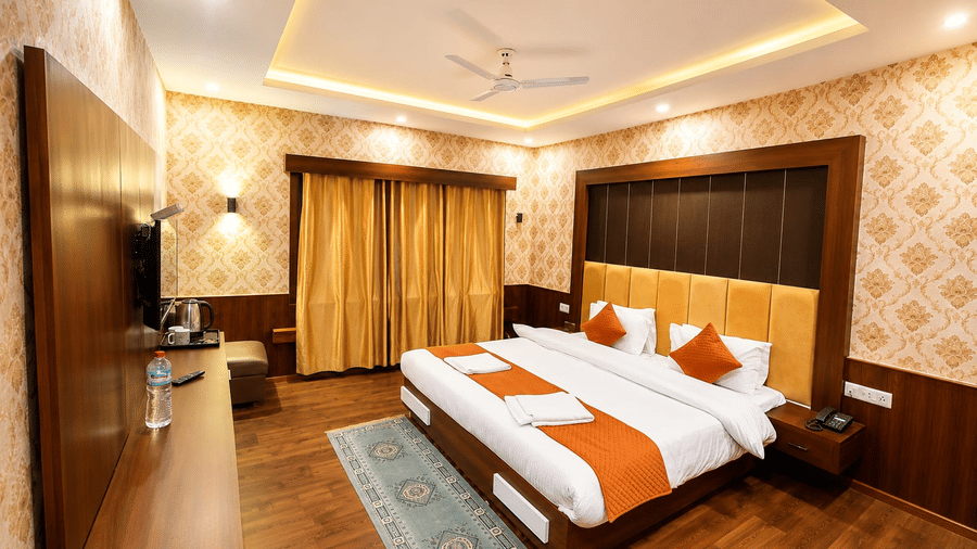 An Executive Room bedroom at Hotel Outlook, Pahalgam, showing a large double bed, wooden wall panels, a desk area, window curtains, and a patterned rug.