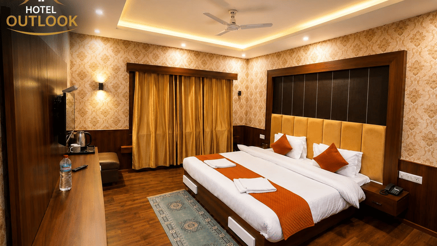 View of a guest bedroom at Hotel Outlook, Pahalgam, featuring a double bed, wallpapered walls, window curtains, and a long wooden console table.