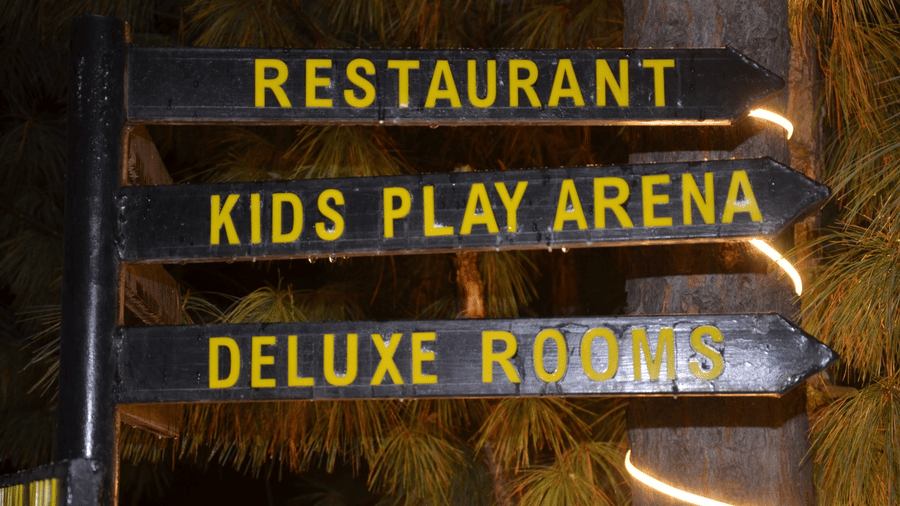 A signpost at Dawat e Drung by FrozenFall Resort, Drung, Tangmarg, with 3 directional arrows for a restaurant, kids play arena, and Deluxe Rooms.