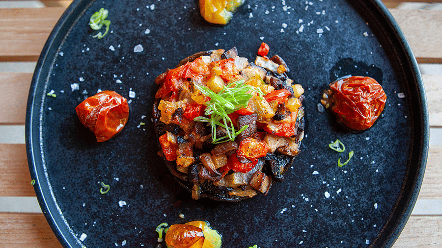 Cooked portobello mushroom stuffed with diced vegetables and topped with fresh herbs on a dark plate at YO1 Longevity & Health Resorts